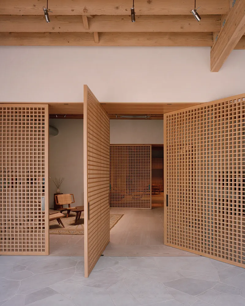 Timber lattice partition walls with square grid openings framing a seated area beneath a beam ceiling with track lighting