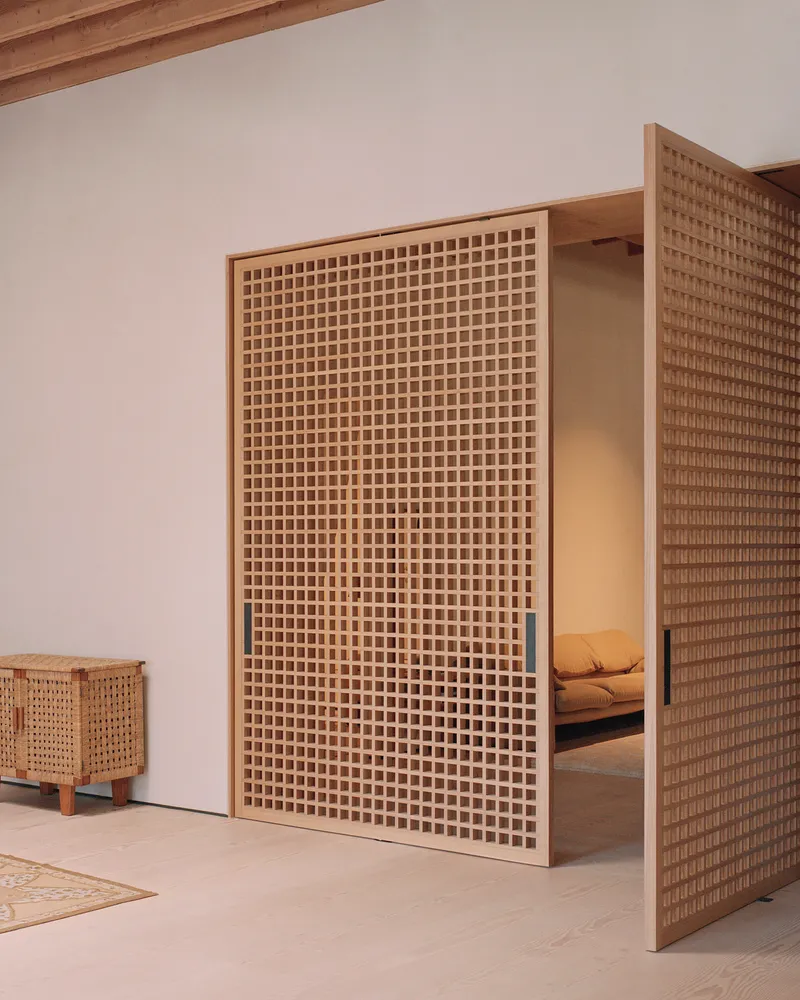 Close-up of a tall timber lattice screen with visible bedroom space beyond a narrow opening in the white wall