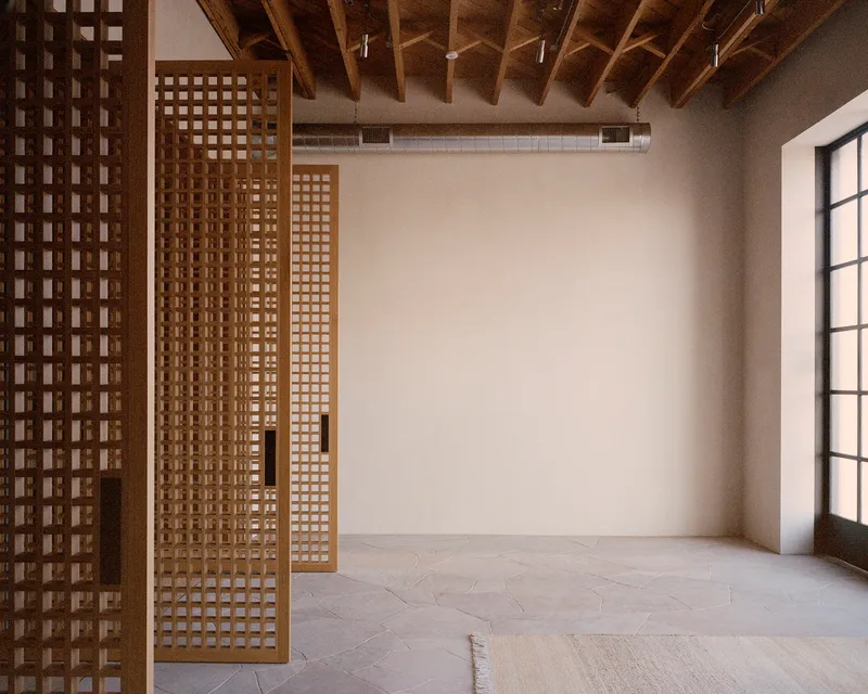 Interior space with latticed timber screens, exposed beam ceiling, and light stone flooring near a steel-framed window