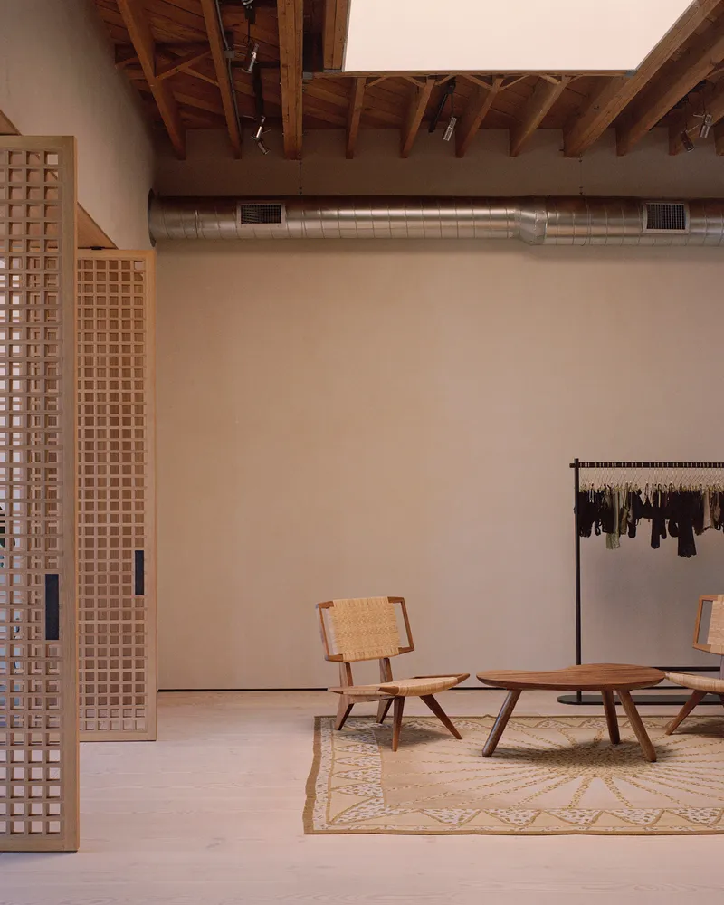 Retail interior with latticed timber partitions, exposed ductwork, timber furniture, and clothing rack on patterned rug