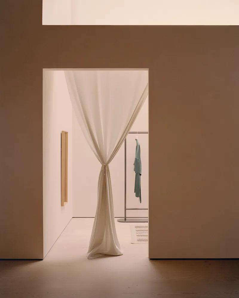 Doorway framed in warm brown walls with draped linen curtain tied back, revealing clothing rack beyond