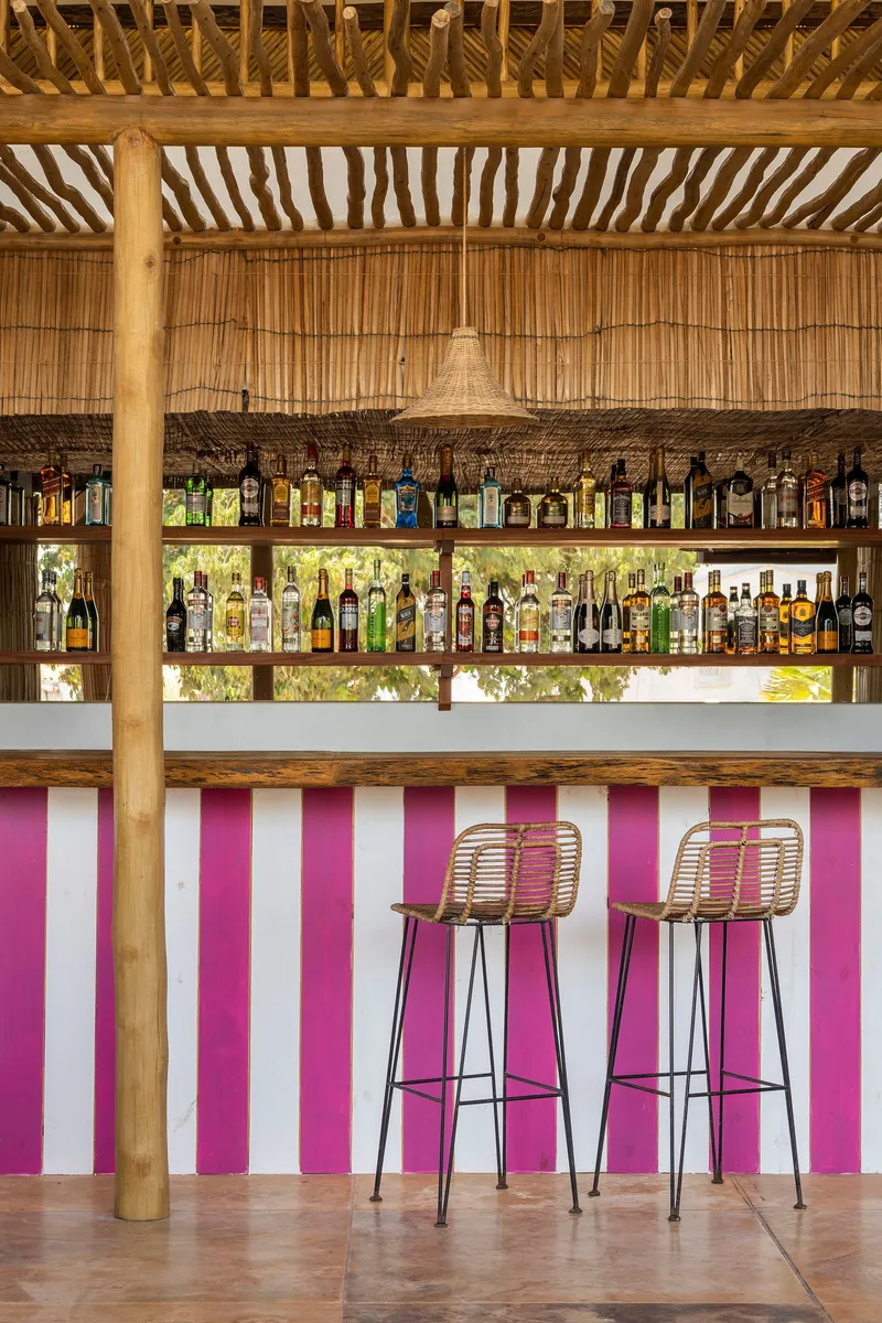 Bar counter with pink and white vertical striped front panel under bamboo ceiling with exposed timber structure