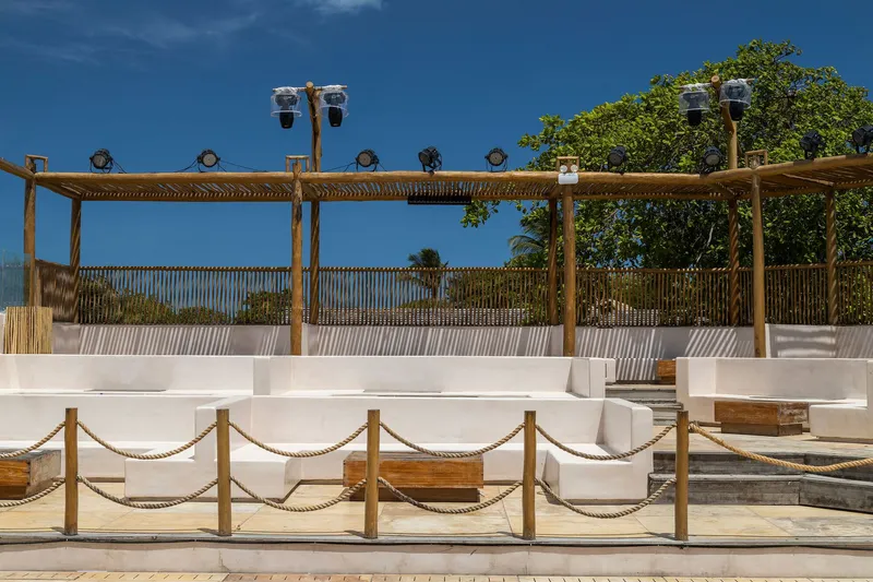 Tiered white concrete seating with rope railings beneath timber pergola and theatrical lighting fixtures