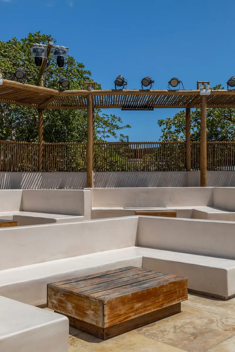 Stepped white concrete seating around reclaimed timber table under timber pergola with bamboo screen backdrop