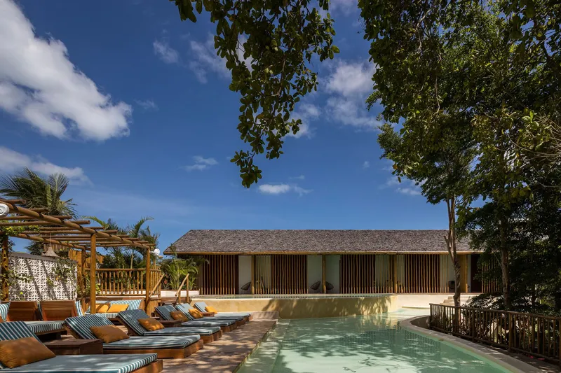 Pool deck with striped loungers facing a pavilion with vertical timber screening under a tiled roof