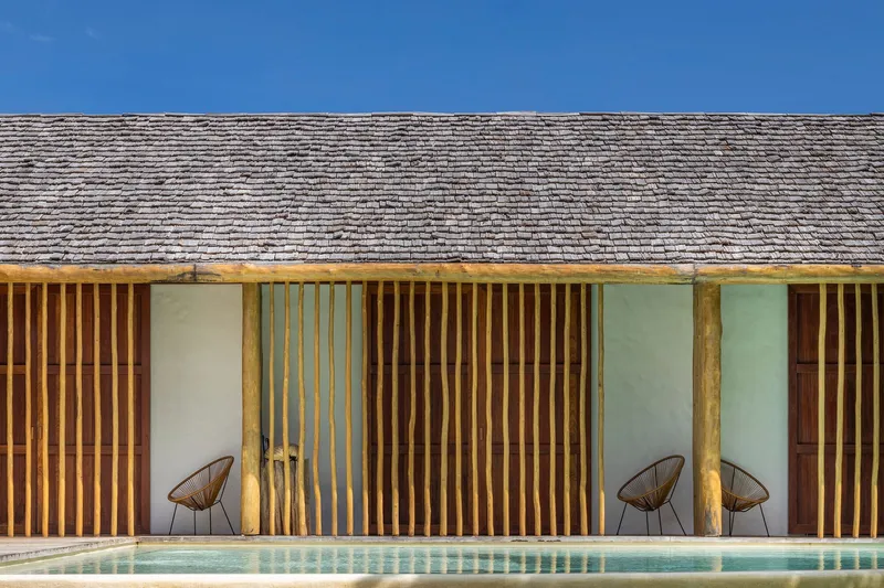 Facade detail of vertical timber louvers alternating with white stucco bays beneath a weathered shingle roof