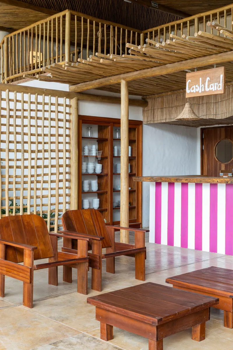 Interior seating area with timber furniture, lattice screen wall and pink-striped counter under exposed bamboo rafters
