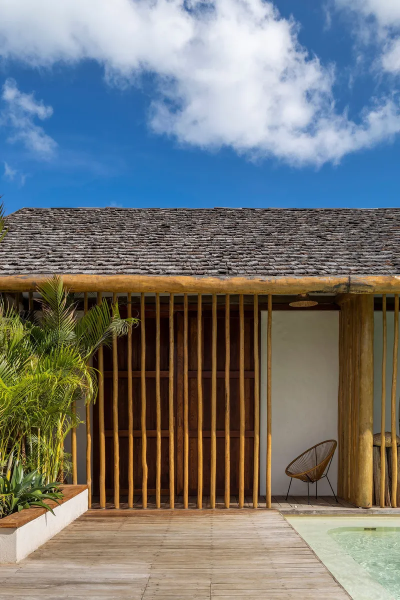 Poolside pavilion with vertical timber slat screen and shingled roof under a bright blue sky
