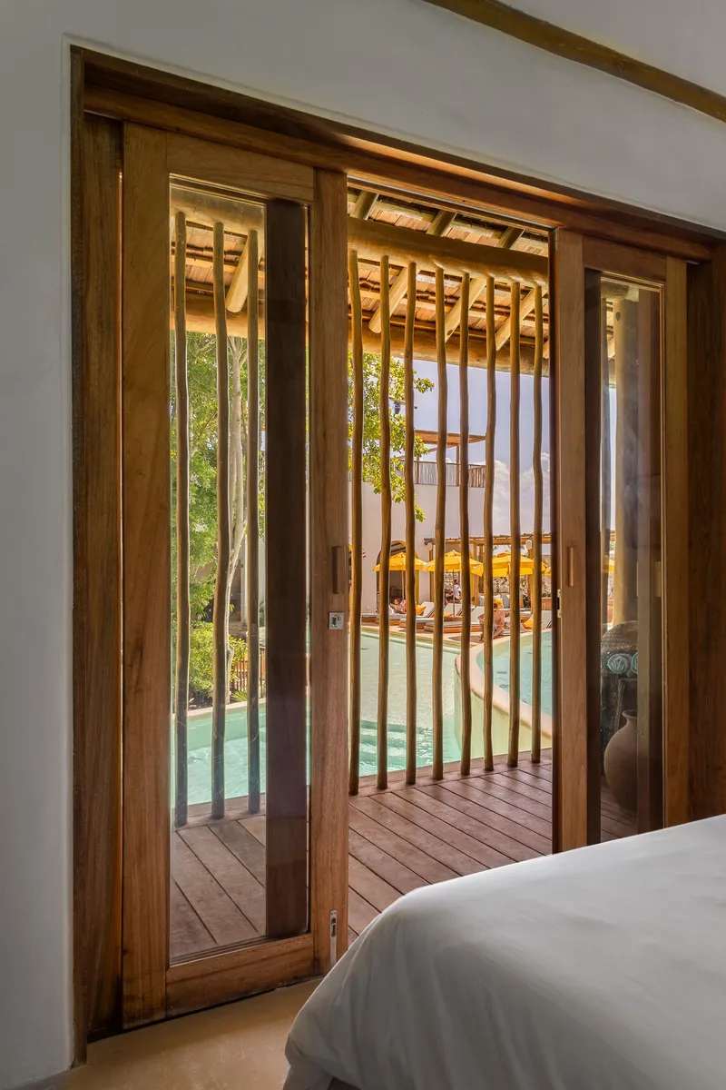 View through sliding timber doors from bedroom to wooden deck and pool beyond with exposed rafters above