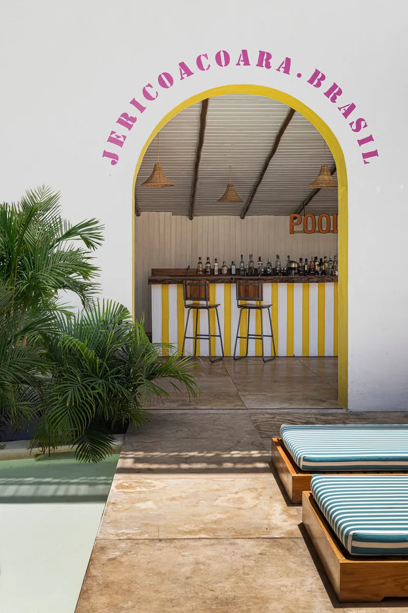 Arched bar opening with yellow frame and striped counter flanked by striped loungers poolside