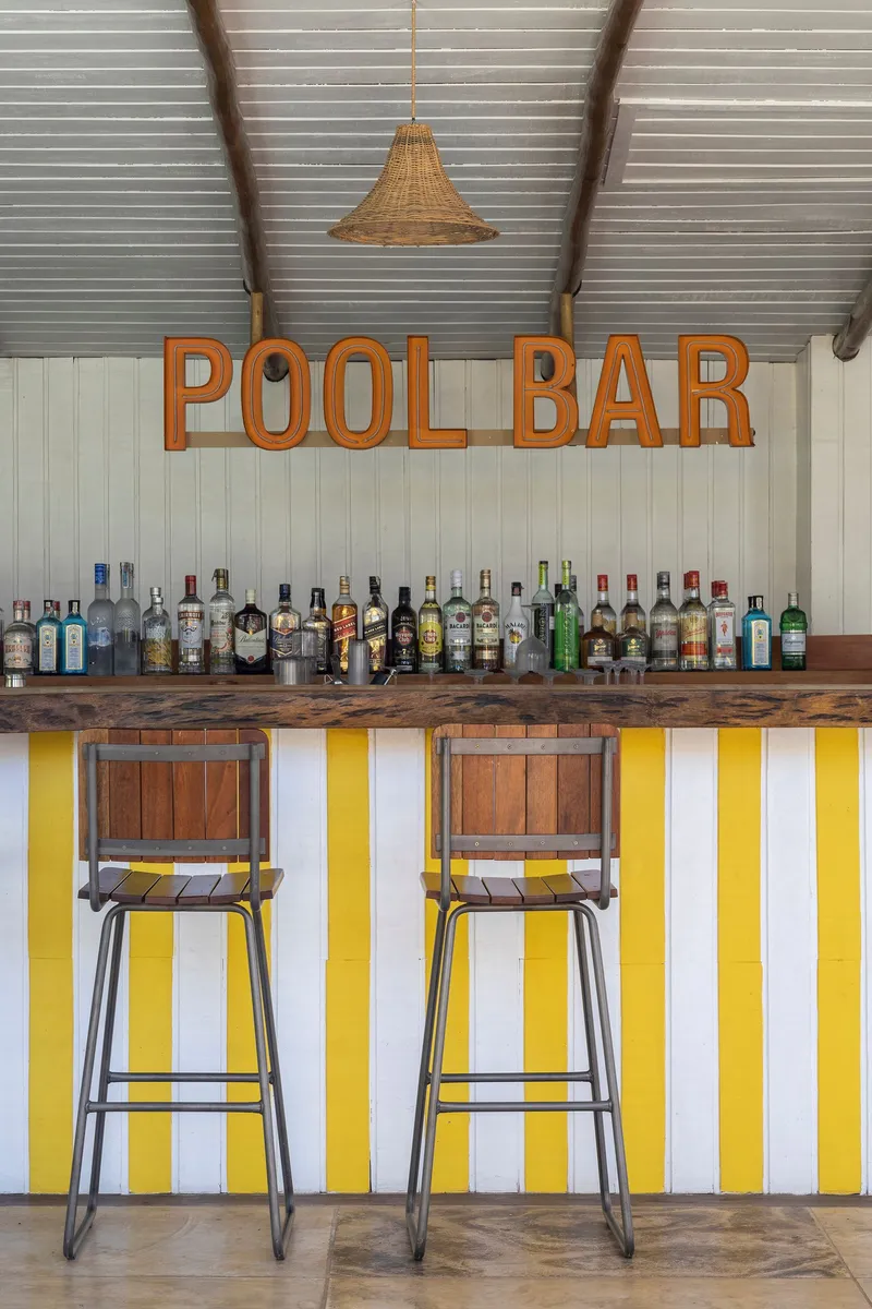 Bar counter with yellow and white vertical striped front panel beneath metal stools and woven pendant light