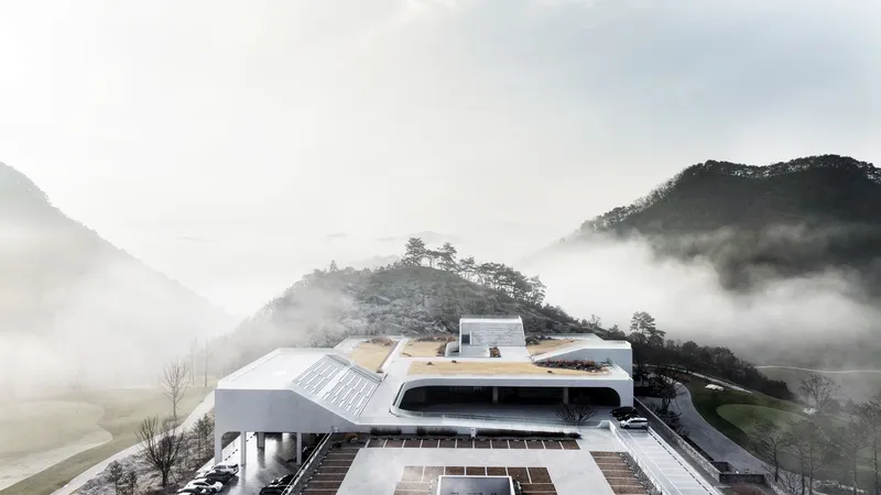 The layered building with curved rooflines and vegetated terraces surrounded by morning mist in the valley
