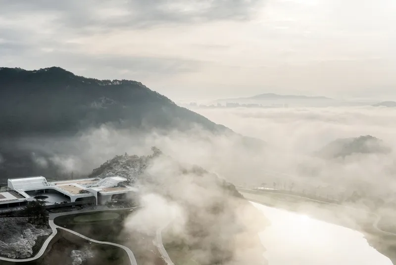Aerial view of the curved rooflines and terraced landscape emerging from dense morning fog