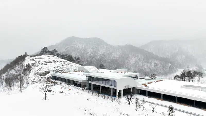 Winter view of the horizontal wings with glazed facades and white roofs stretching across the snowy hillside
