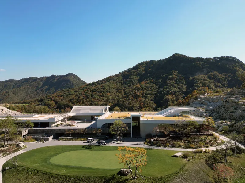 Elevated view of the complex with curved roofs and a circular lawn terrace surrounded by mountains in daylight