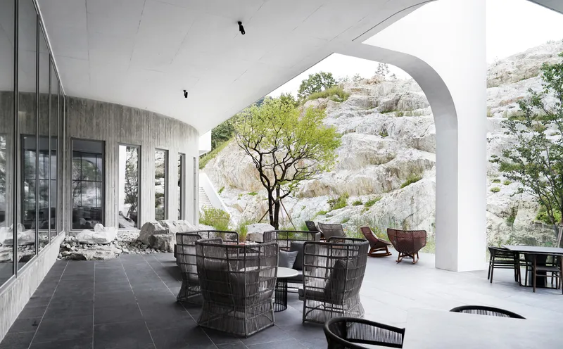 Covered terrace with vaulted white ceiling and dark wicker furniture framed by a large arch opening to rocky hillside