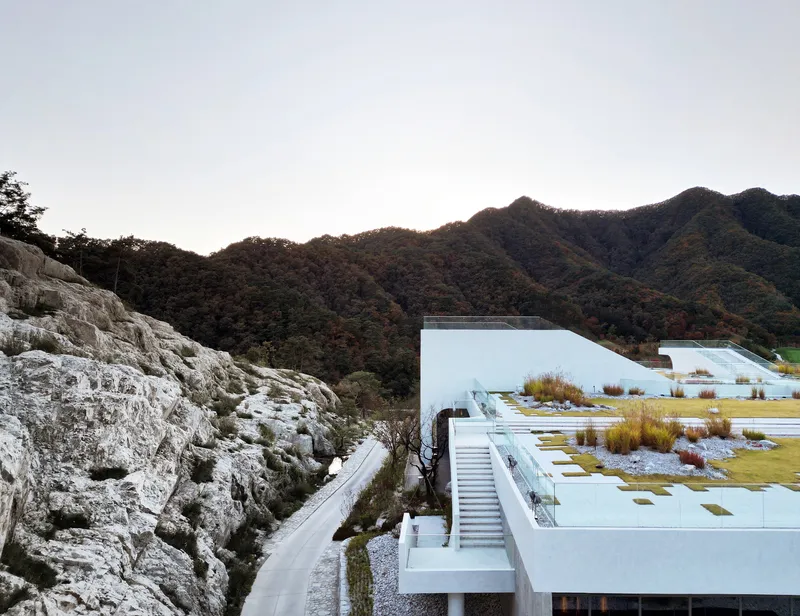 Planted roof terraces stepping down the rocky hillside with forested mountains in the background at dusk
