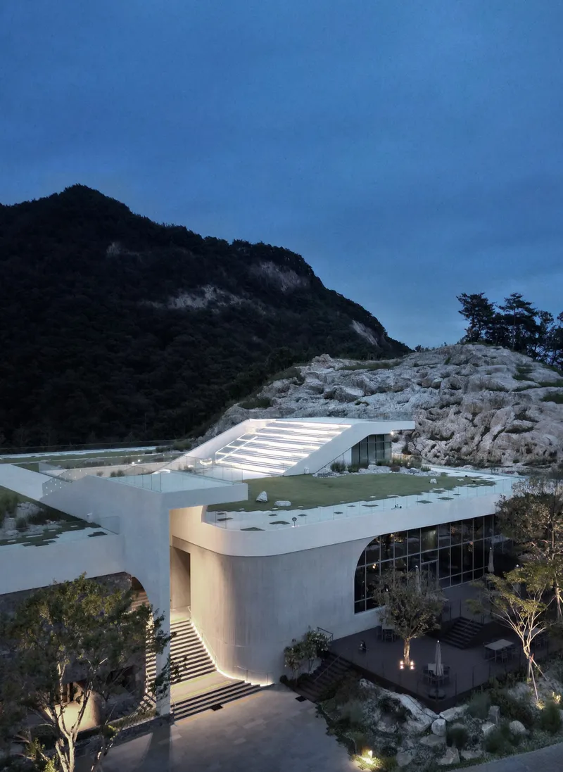 Elevated view of the illuminated entrance volume with curved glass facade and ribbed roof at twilight