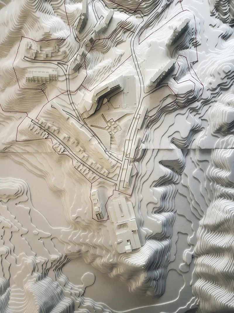 Physical topographic model with layered contours showing building volumes carved into rolling terrain