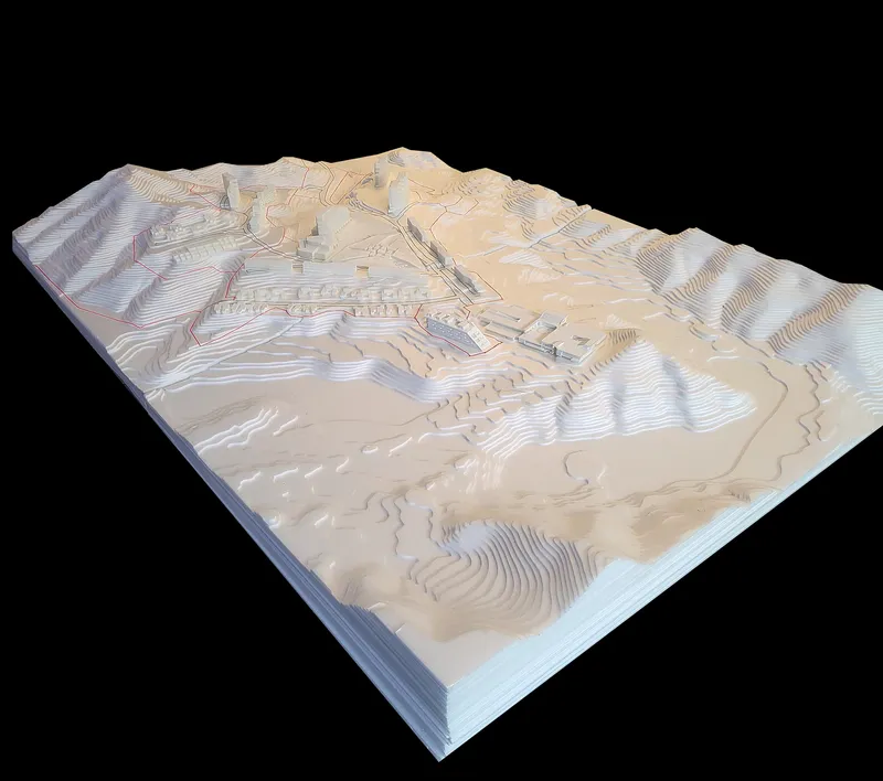 The image shows a detailed architectural model of a site plan, emphasizing the topography and landscape. The model is constructed in layers, revealing contour l
