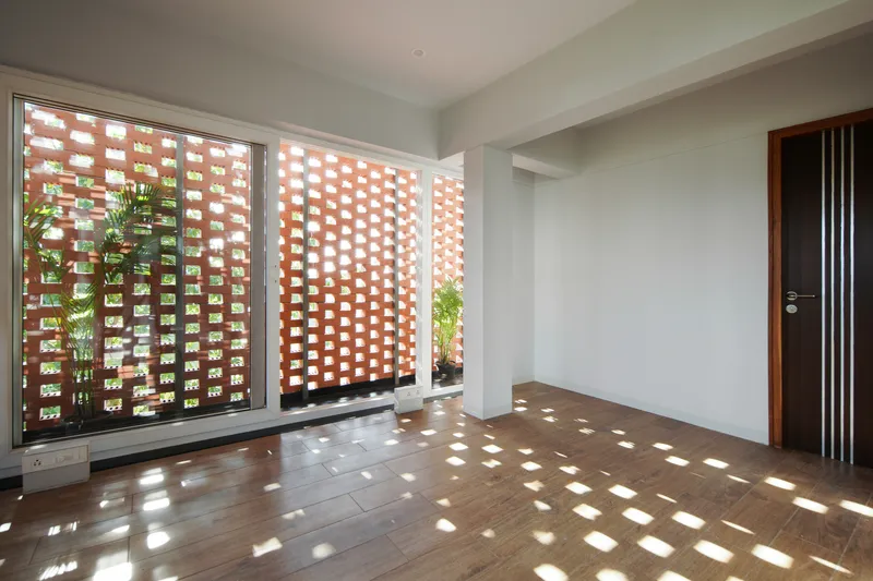 Interior room with perforated brick screen wall casting dappled light patterns across the timber floor