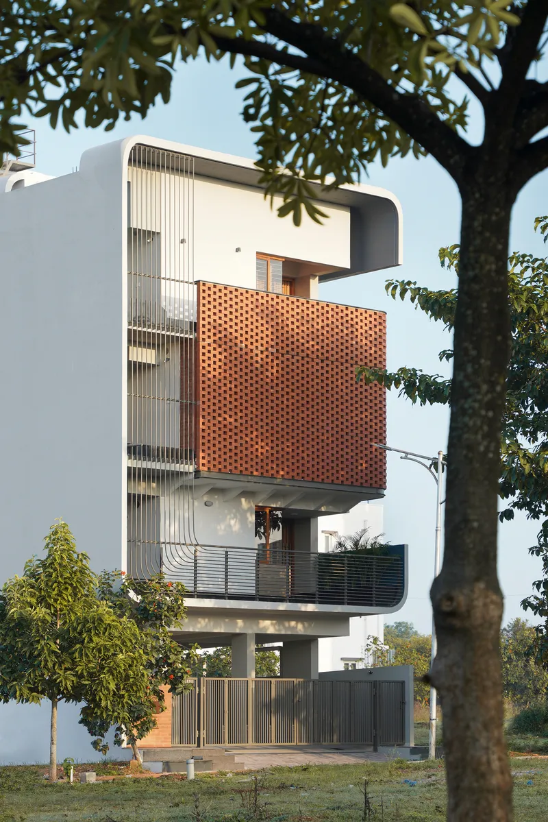 Street view of the stacked facade with perforated brick screen seen through mature tree foliage at dusk