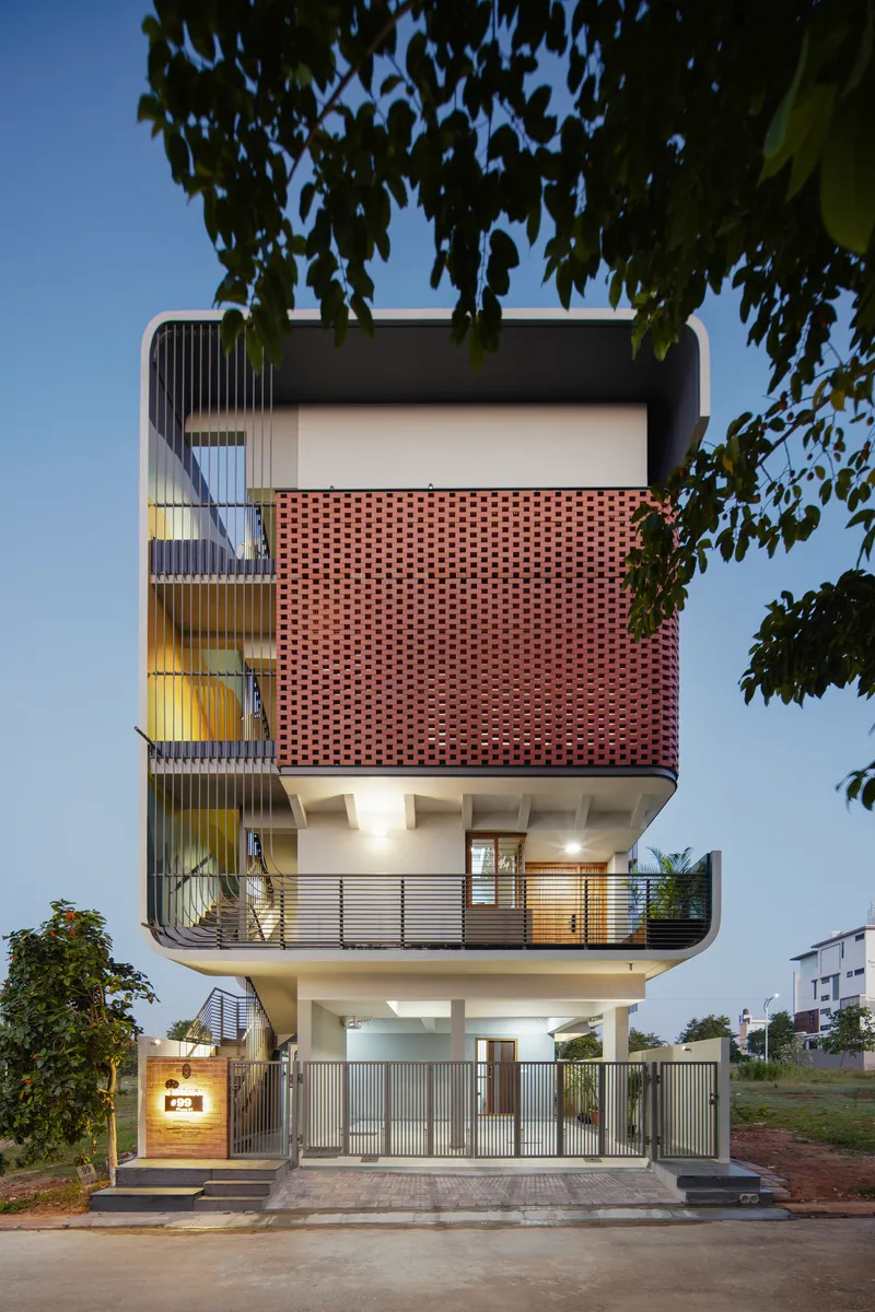 Street elevation showing the stacked volumes with perforated terracotta brickwork screen and cantilevered balconies at dusk
