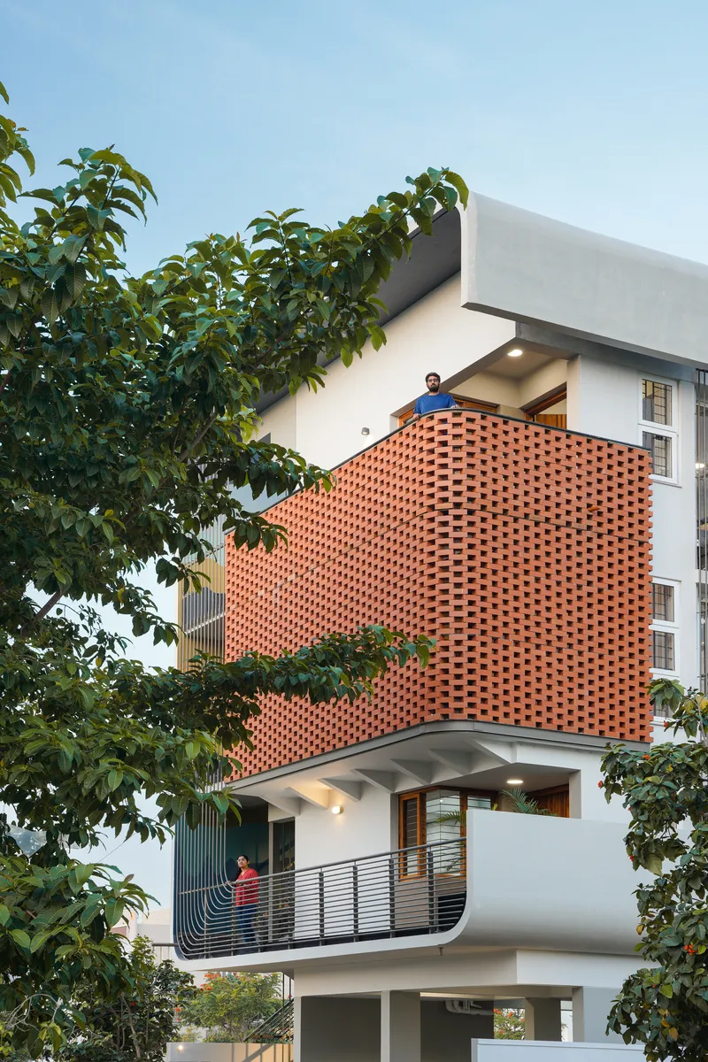 Facade detail of the perforated brick screen with residents on the curved balconies framed by foliage