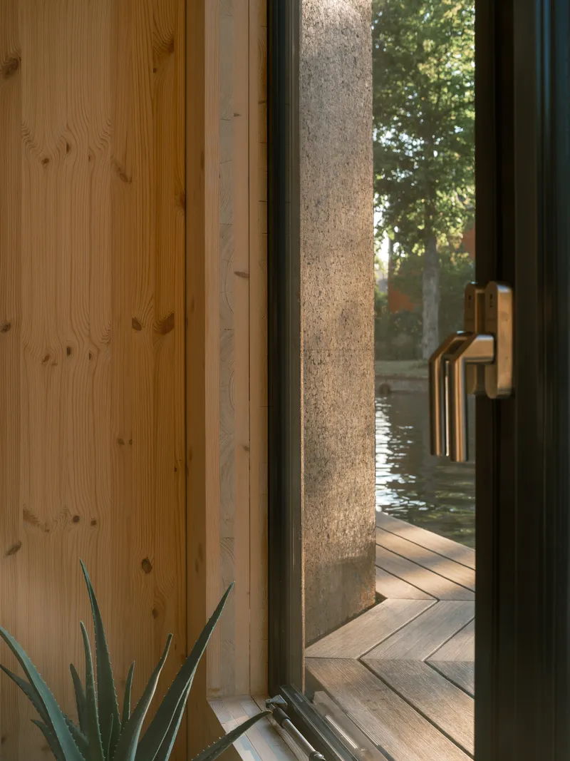 Glazed door with brass handle opening to a timber deck beside a hempcrete wall at dusk