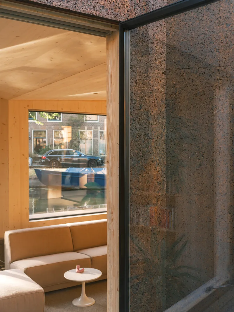 Corner threshold between interior pine paneling and exterior hempcrete facade with street view through glazing