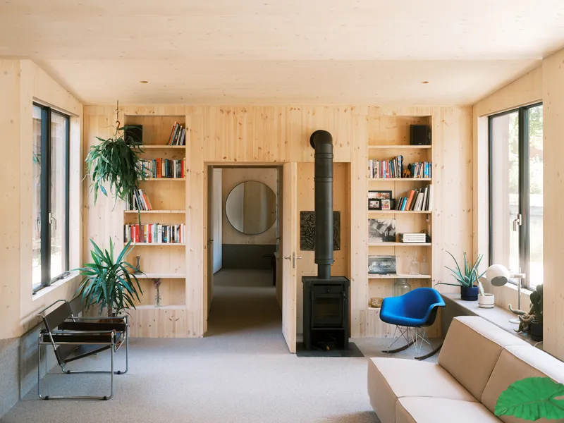 Living room with light timber paneling, built-in shelving, and freestanding wood stove flanked by glass doors