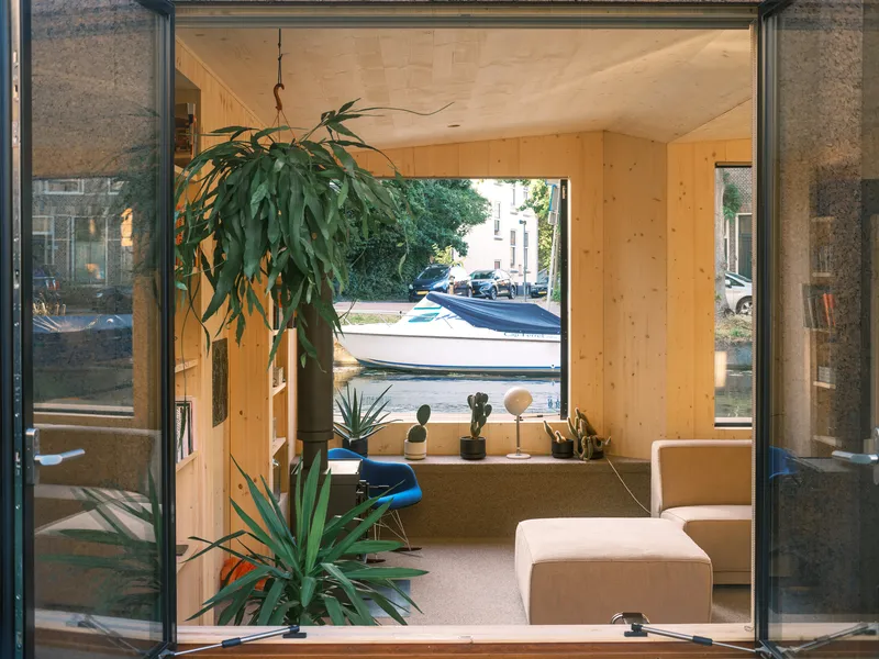 View through open glass doors toward the canal with hanging plants and moored boats visible outside