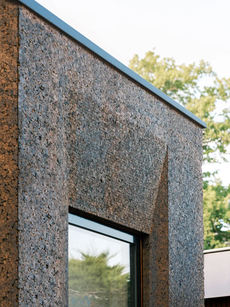 Close-up of the cork cladding panel joint and metal cap edge with trees visible beyond