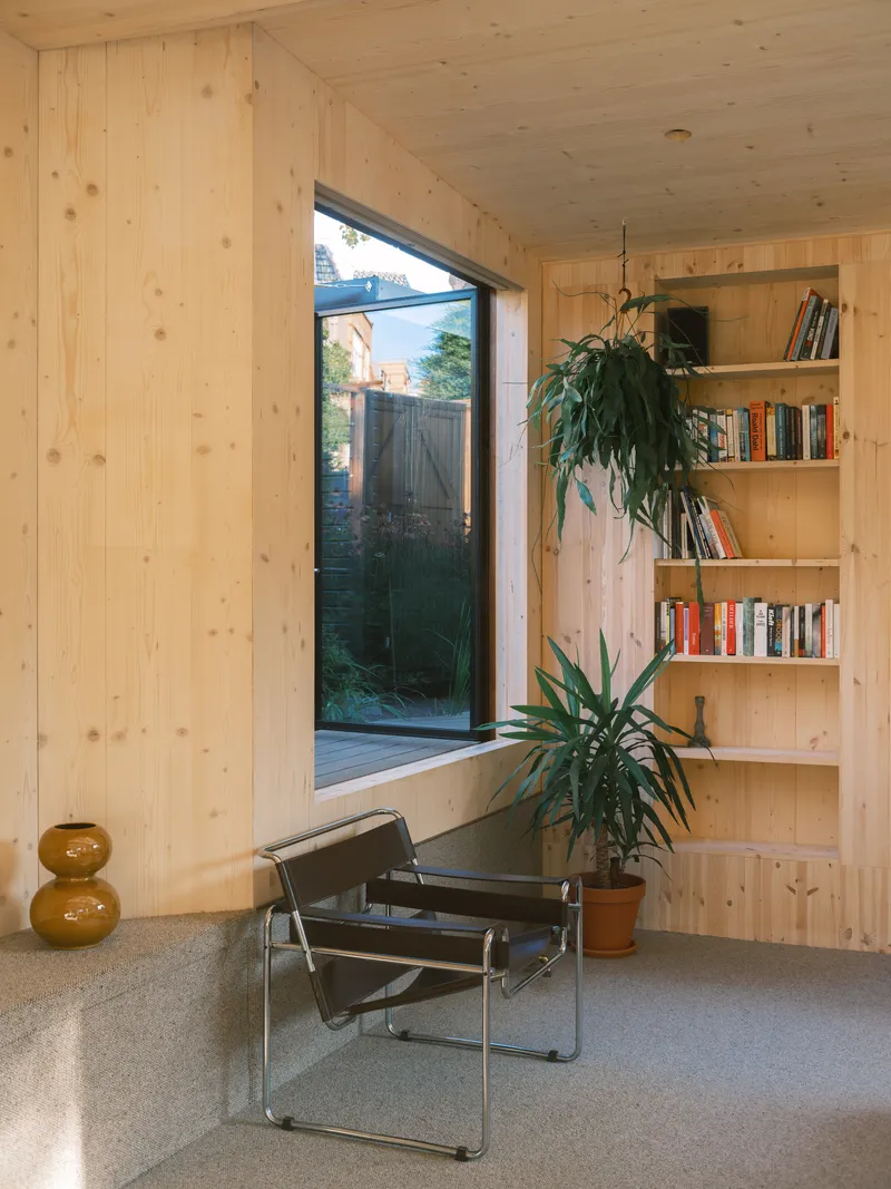 Interior corner with pine-clad walls, built-in shelving, and leather chair beside a full-height window