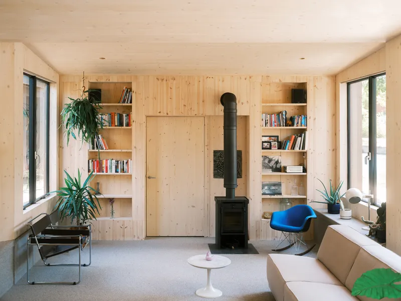Light timber living room with built-in bookshelves flanking a central wood stove and flush door