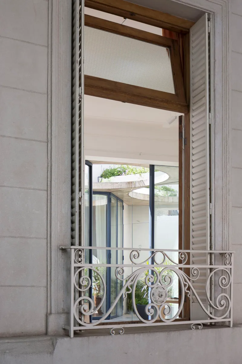 Open window with ornamental wrought iron balcony railing and timber frame looking into a planted courtyard