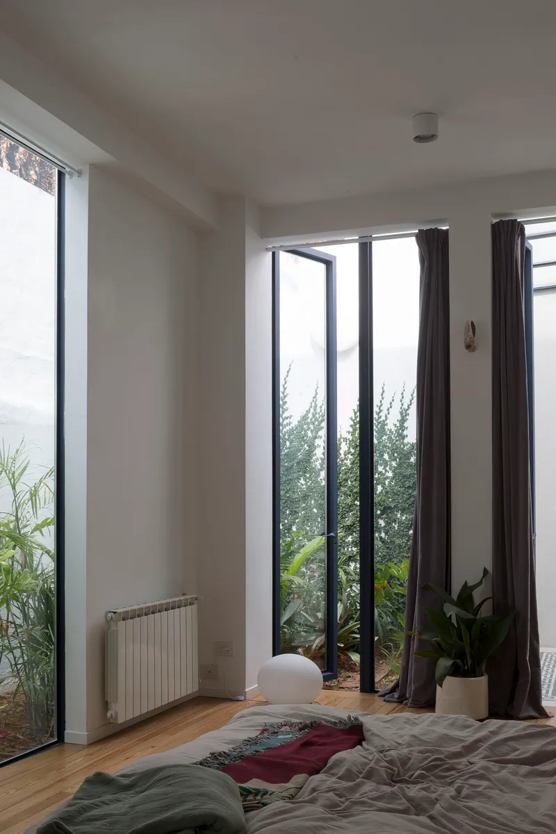 Bedroom with floor-to-ceiling glazing framing a planted lightwell and oak flooring below white walls