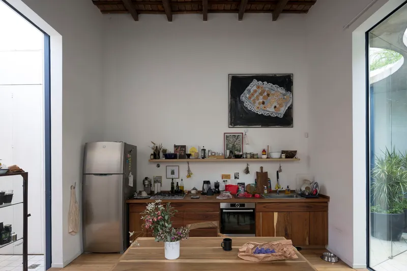 Kitchen with exposed timber beam ceiling, walnut cabinetry, and openings to planted courtyards on both sides