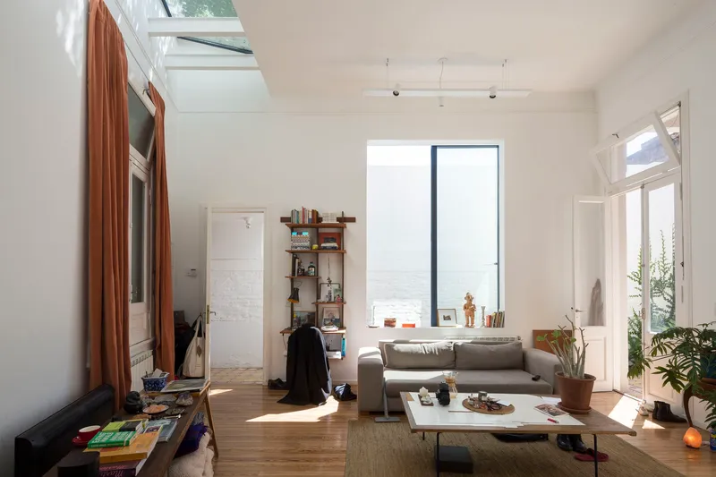 Living room with timber flooring and tall window framing a view of the sea in bright daylight