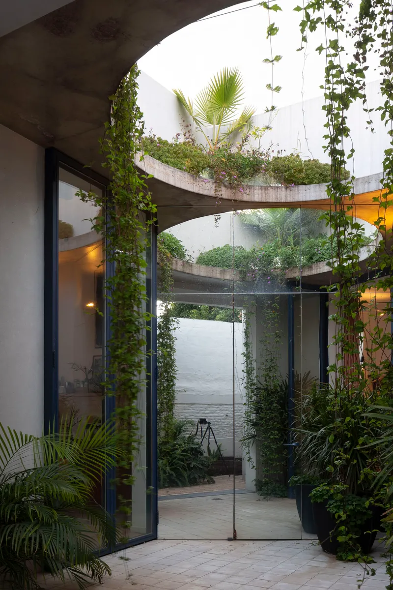 Interior courtyard with spiraling concrete planters wrapped in climbing vines and potted palms below