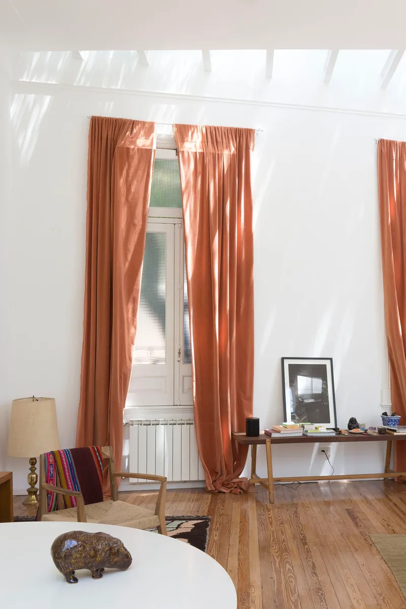 Interior room with terracotta curtains and sloped skylight ceiling casting sharp shadows across the floor