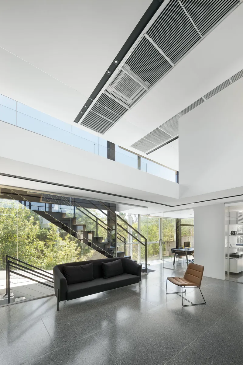Double-height lobby with diagonal staircase, terrazzo flooring and linear ceiling grilles above