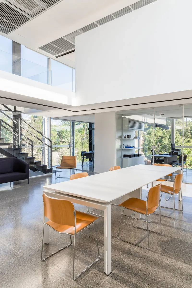 Double-height dining area with white table, steel staircase and integrated ceiling grilles