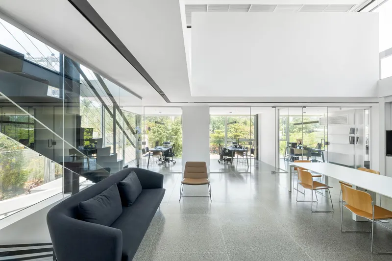 Open-plan workspace with full-height glazing overlooking gardens and a glass-walled staircase at left