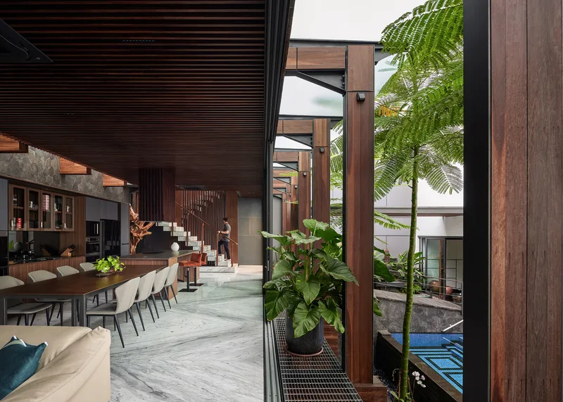 View from the open living space through timber columns toward the planted courtyard and pool