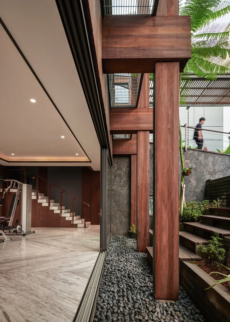Vertical timber slat screen beside an interior courtyard with black river stones and a figure on the upper level