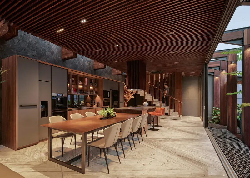 Open dining area beneath a slatted timber ceiling with staircase and living space beyond