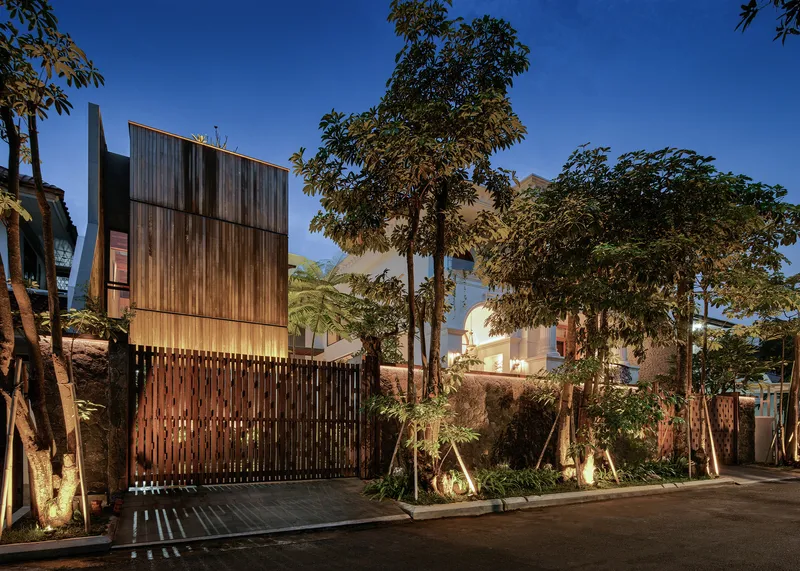 Street view of the timber facade and vertical slat fence screened by trees at dusk