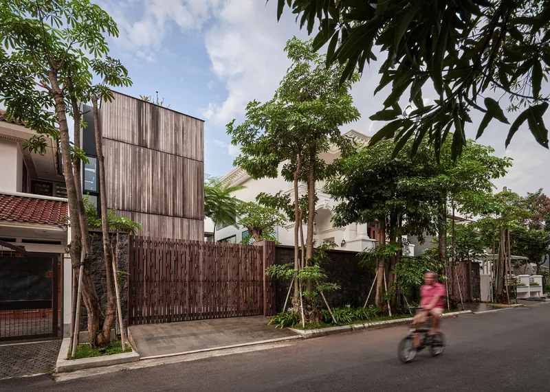 Street view of the vertical timber-clad volume behind a slatted wooden fence with a cyclist passing by