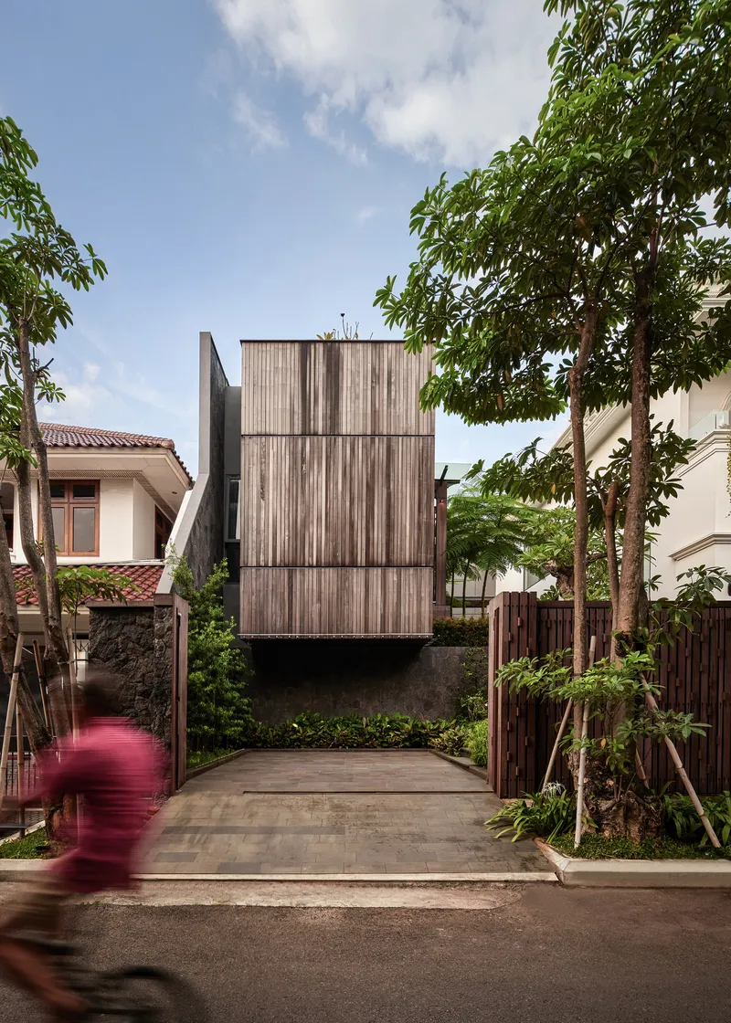 Entrance courtyard showing the cantilevered timber box above a stone wall with a cyclist in motion